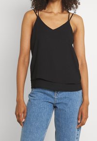 Black sleeveless top with a V-neck design, made from lightweight fabric, featuring thin straps and a layered hem, paired with blue jeans.