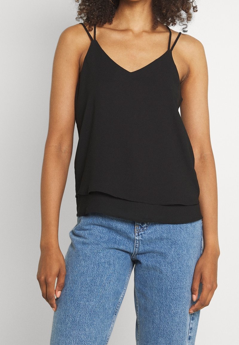 Black sleeveless top with a V-neck design, made from lightweight fabric, featuring thin straps and a layered hem, paired with blue jeans.