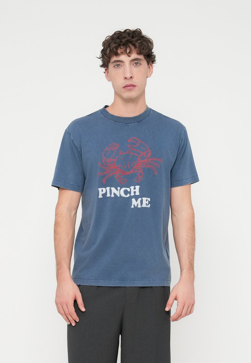 Μπλε βαμβακερό T-shirt με κοντά μανίκια και στρογγυλή λαιμόκοψη. Διαθέτει κόκκινο γραφικό καβούρι και το κείμενο "ΤΣΙΜΠΗΣΤΕ ΜΕ" σε λευκό χρώμα.