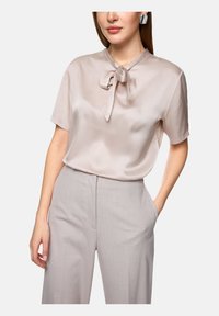 Silk blouse in soft beige with a bow tie at the collar, paired with light gray tailored pants featuring side pockets.