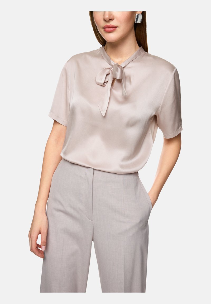 Silk blouse in soft beige with a bow tie at the collar, paired with light gray tailored pants featuring side pockets.
