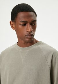 Slim fit, lys grå sweatshirt med struktureret stof. Har en rund halsudskæring og raglanærmer, som viser subtile sømdetaljer.