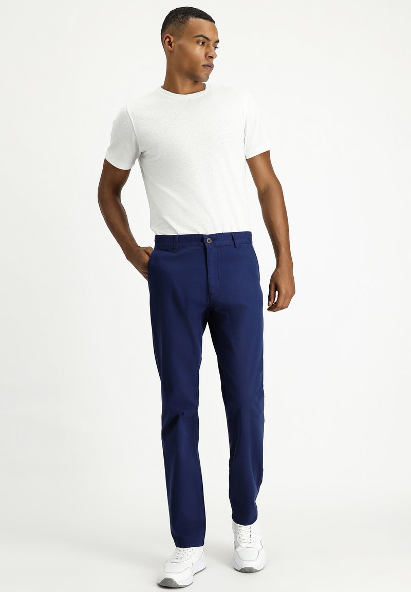 Pantalones azul marino de corte ajustado, hechos de una tela suave, con cierre de botón y bolsillos laterales, combinados con una camiseta blanca.