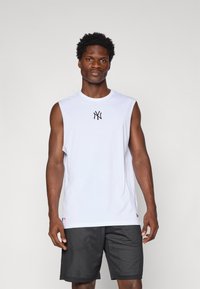 T-shirt sans manches blanche avec le logo NY noir sur la poitrine ; associée à un short en mesh noir, mettant en valeur une coupe athlétique et une texture respirante.