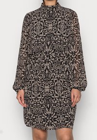 Svart blommönstrad klänning med långa ärmar och hög krage. Tillverkad av genomskinligt tyg, har en åtsittande midja och en avslappnad passform.