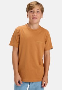 Polo tričko s krátkym rukávom a okrúhlym výstrihom v spálenej oranžovej farbe, s malým žltým logom na hrudi a čiernou nášivkou na rukáve.