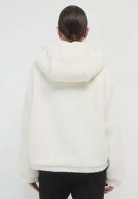 Felpa bianca in pile con superficie morbida e testurizzata, vestibilità oversized e un ampio cappuccio. Presenta polsini elasticizzati e un orlo dritto.