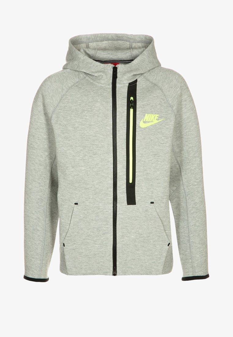 Grijs gewatteerd jack van zachte stof. Voorzien van een zwarte ritssluiting, twee steekzakken aan de voorkant en een neongele logo op de borst.