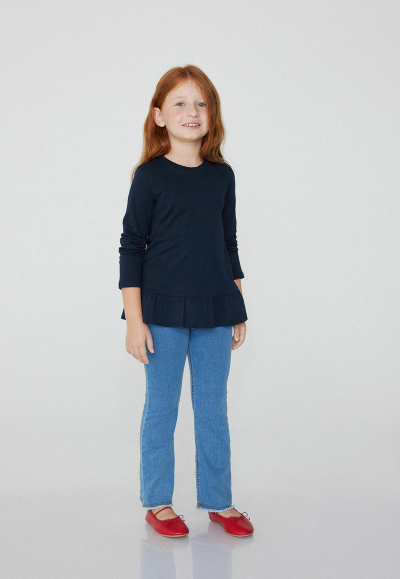 Granatowa bluzka z długim rękawem i peplum, połączona z jasnoniebieskimi dżinsami o prostym kroju oraz czerwonymi balerinami z akcentem w postaci kokardki.