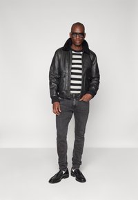 Chaqueta bomber de cuero negro con cuello de piel, suéter de rayas en blanco y negro, jeans ajustados grises y zapatos de vestir negros.