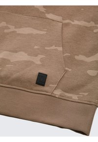 Hoodie beige avec un motif camouflage dans des teintes plus claires, des poignets côtelés, et un petit écusson noir près de la couture de la poche.