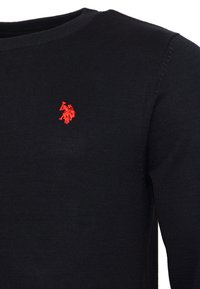Primo piano di un maglione nero a maglia con logo ricamato rosso di un polo player su cavallo sul petto, mostrando il collo e parte della manica.