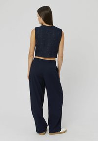 Top sans manches cropped bleu marine avec une finition texturée, associé à un pantalon large bleu marine, présentant un tissu lisse et des poches arrière discrètes.