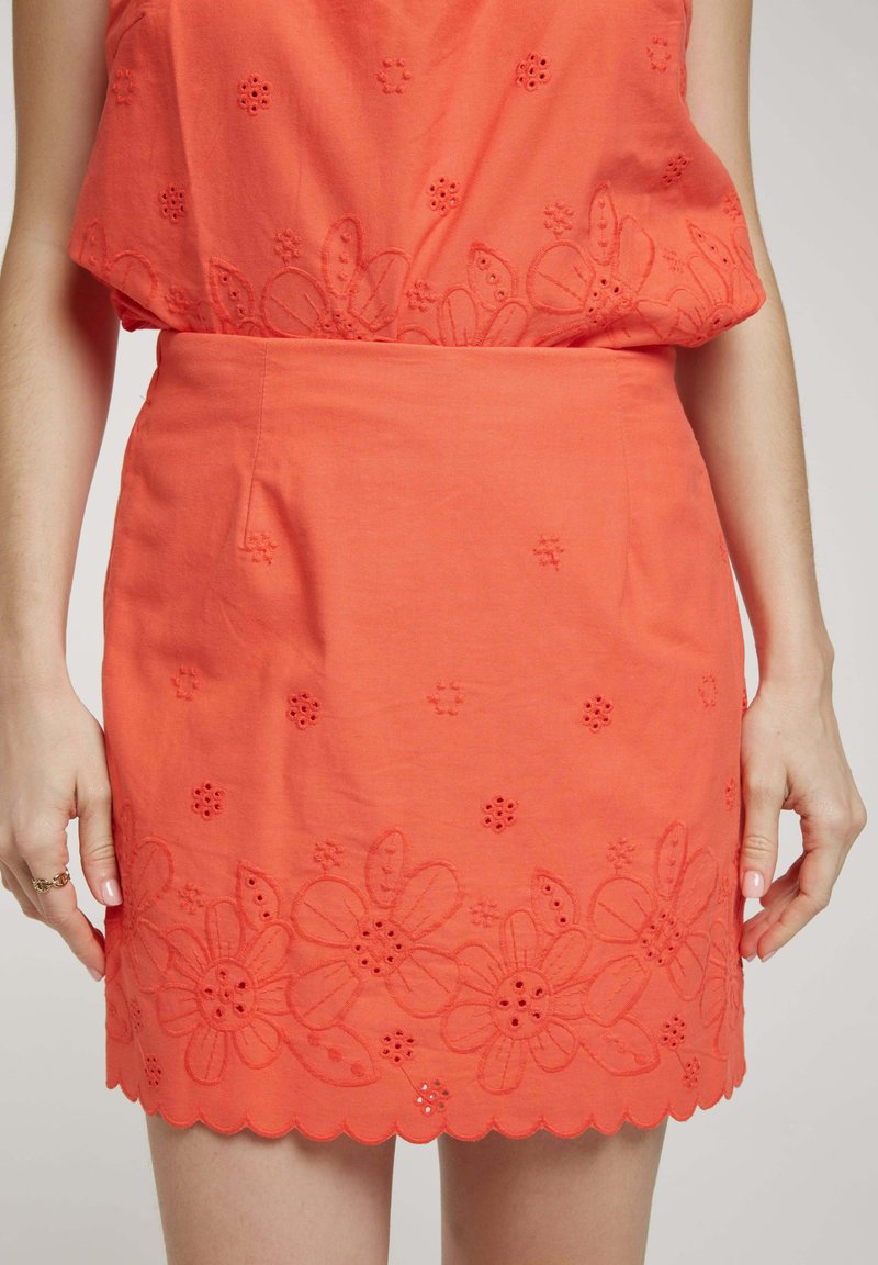 Jupe corail avec broderies florales et découpes le long de l' ourlet. Design droit, longueur mi-cuisse, fabriquée à partir d'un tissu léger.