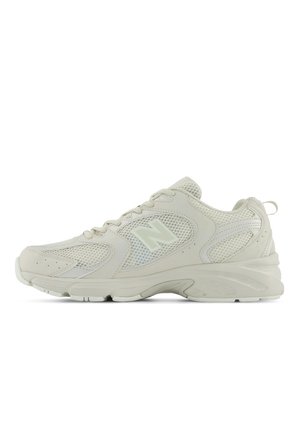 Lys beige atletisk sneaker med mesh-paneler, snøredesign, polstret sål og et diskret "N"-logo på siden.
