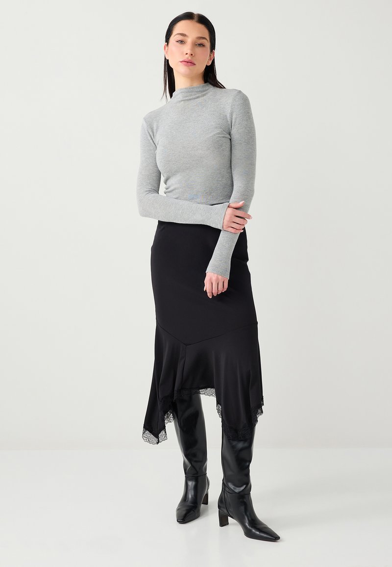 Pull gris clair ajusté à col roulé associé à une jupe asymétrique noire ornée de dentelle et des bottes noires montantes à talon carré.