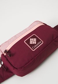Bordo platnena vrećica s ružičastim detaljima, koja ima središnju zip zatvarač, teksturiranu površinu i oznaku logoa Columbije.