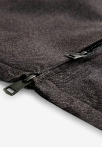 Black fabric with a smooth texture, featuring a visible zipper and metal pull tab. Close-up view emphasizes stitching and fabric detail.