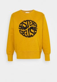 Sudadera amarilla con texto redondo negro "SISTERS" en una fuente retro. Cuenta con cuello redondo y puños acanalados. Textura suave.