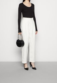 Top nero a coste con maniche lunghe, pantaloni bianchi a vita alta, borsa nera con tracolla a catena e décolleté neri a punta. Texture lisce, vestibilità moderna.