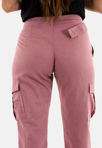 Pantalones cargo sueltos de tejido rosa polvoriento, con bolsillos laterales y un detalle de solapa en la parte posterior. Diseño simple y texturizado.