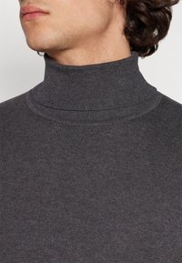 Grå ribbatröja med hög krage och slät textur, designad med en åtsittande siluett och minimalistisk stil.