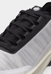 Κοντινό πλάνο ενός γκρίζου και μαύρου αθλητικού παπουτσιού με υφασμάτινο επάνω μέρος με υφή, μαύρα κορδόνια και ένα λογότυπο στη γλώσσα.