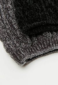 Zwei strukturierte Stoffstücke, eines schwarz und eines grau, die ein plüschiges, geripptes Oberflächenmuster zeigen. Beide haben abgerundete Kanten und eine weiche Oberfläche.