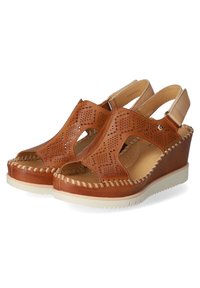 Wedge in pelle marrone con design perforato, apertura davanti e cinturino sul retro. Presenta dettagli di cucitura e una suola in gomma bianca per ottima aderenza.