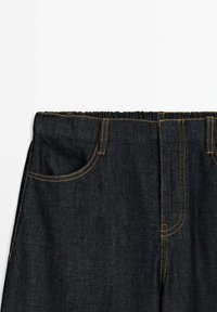 Tmavé džínové kalhoty s elastickým pasem, předními kapsami a kontrastním žlutým šitím podél švů. Hladká textura.