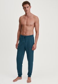 Teal pyjamabroek met een trekkoord in de taille, taps toelopende benen en ribbels aan de enkels. Zachte textuur van de stof; geen patronen of extra accenten.
