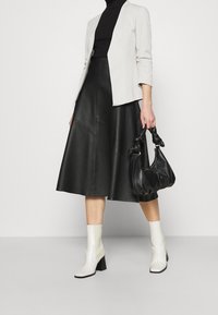 Czarna skórzana spódnica midi, dopasowana biała marynarka, czarna torebka i białe botki na słupku. Gładkie faktury, czyste linie.