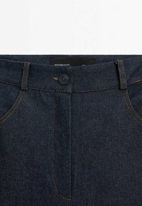 Jean en denim bleu foncé avec une texture lisse, présentant des surpiqûres orange, une fermeture à bouton, et une étiquette indiquant "Massimo Dutti".