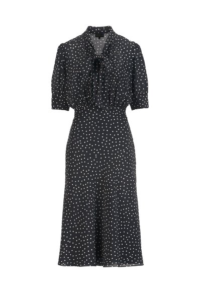 Črna obleka z belimi pikami, ki ima ovratnik z mašnico, kratkimi nabranimi rokavi in razširjenim krilom. Tkanina je videti lahka in gladke teksture.