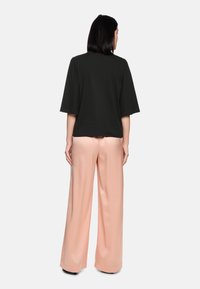 Black short-sleeve top paired with loose, pale pink wide-leg trousers. Smooth fabric with a relaxed fit, emphasizing a clean silhouette.