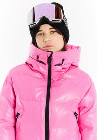 Helle pinke Daunenjacke mit hohem Kragen, schwarzem Reißverschluss vorne und seitlichen Taschen. Kombiniert mit Skibrille und einer schwarzen Strickmütze.