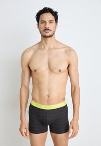 Black boxer shorts with a textured pattern, featuring a bright yellow waistband with "PUMA" logo repeated. Fitted design, soft material.