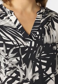 Svart-vit blus med ett bladmönster, mjukt tyg, v-ringad design och korta ärmar med avslappnad passform.