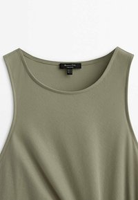 Débardeur vert olive sans manches avec encolure ronde, fabriqué en tissu doux avec une finition texturée. L'étiquette indique les détails de taille dans plusieurs régions.