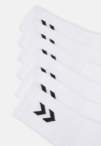 Fehér zoknik bordázott textúrával, fekete chevron mintákkal a szárakon. Lélegző anyagból készült, alkalmas sportoláshoz.