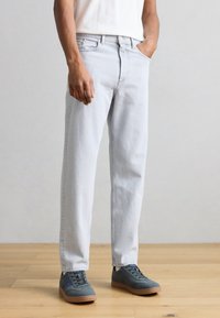 Svetlomodré denimové džínsy s voľným strihom, dizajnom s piatimi vreckami a zapínaním na gombíky, v kombinácii so sivými teniskami a bielou košeľou.