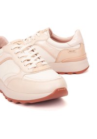 Zapatillas de deporte en crema y beige con cordones, suelas de goma texturizadas y etiqueta de la marca Pikolinos en el lado y en la lengüeta, presentadas sobre un fondo blanco.