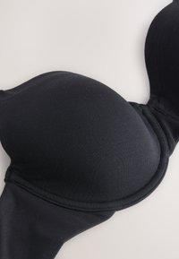 Soutien-gorge noir rembourré avec armatures, tissu lisse et bonnets moulés posé à plat sur une surface claire.