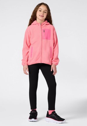 Felpa rosa in pile con zip e tasca frontale, abbinata a leggings neri e sneakers neri con accenti rosa. Texture morbida, vestibilità comoda.