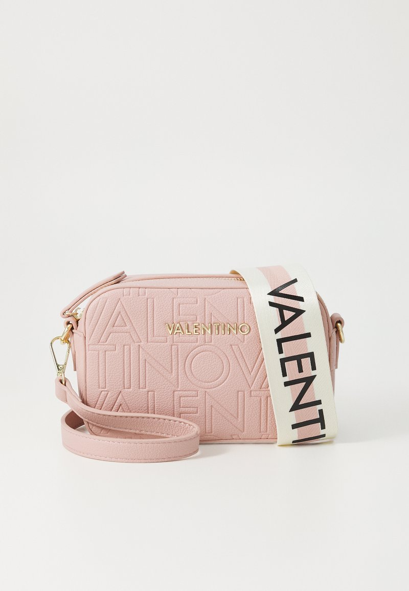 Ružičasta kožna torba preko tijela s urezanim logotipom, zlatnim hardverom i kontrastnim remenom s crnim slovima. Teksturirana završna obrada i zatvaranje na patentni zatvarač.