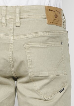 Pantaloni in denim beige con etichetta in pelle con marchio in vita, design a cinque tasche e dettagli di cucitura tono su tono.