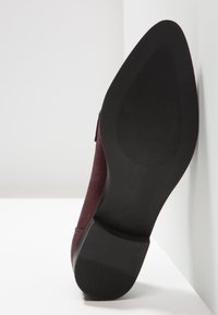 Semelle d'une chaussure bordeaux à bout pointu avec grip en caoutchouc noir texturé sur l'avant-pied et talon rainuré, taille 37 visible sur la semelle.