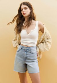 Jasnoniebieskie dżinsowe szorty z wysokim stanem i postrzępionym końcem, w zestawie z białym prążkowanym topem na ramiączkach i beżową, szeroką koszulą w paski.