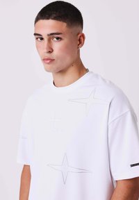 Witte T-shirt met korte mouwen, voorzien van een subtiel sterrenpatroon en geborduurd logo, gemaakt van zachte stof met een ontspannen pasvorm en ronde hals.