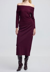 Burgundowa sukienka na ramiączkach z długimi rękawami, dopasowanym korpusem i prostą spódnicą; połączona z błyszczącymi, wysokimi kozakami do kolan.